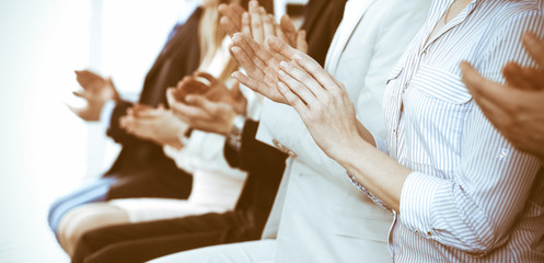 Obraz premium Business people clapping and applause at meeting or conference, close-up of hands. Group of unknown businessmen and women in modern white office. Success teamwork or corporate coaching concept