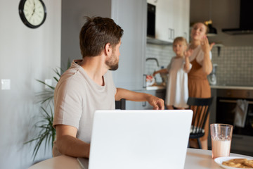 working man turned his head back, looks at his wife and daughter in the kitchen. freelance, work from home concept