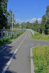 Bike path equipped with fencing, lights, going into the distance. On a Sunny summer day, against a clear blue sky