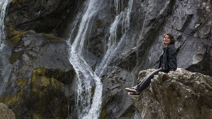 The girl sits on a rock beside a waterfall.