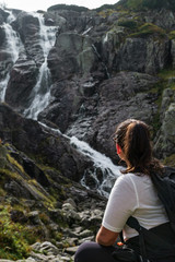 Naklejka na ściany i meble The girl sits on a rock and looks towards the waterfall Wielka Siklawa