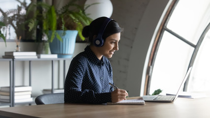 Side view smiling young mixed race employee wearing headphones, improving knowledge on online...