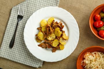 a plate of potatoes with larvae mushrooms on a napkin and a fork next to pickled cucumbers and tomatoes and cabbage.