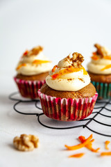 three carrot cake muffin with icing and carrot shaving on cooling rack white background with copy space