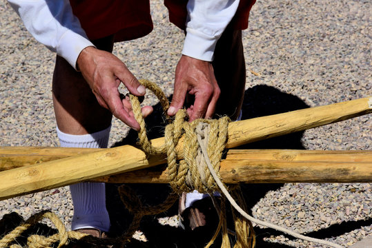 Teepee construction: American Indian man lashes wet rope around the top enes of teepee poles. Wet rope is used and it will tighten as it dries.