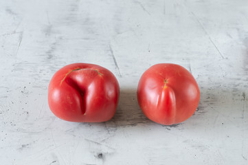 Ugly food, crooked red tomatoes lie on a light concrete background
