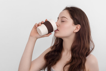 A young girl with long hair drinks from a reusable bamboo cup. Young girl with blue eyes.