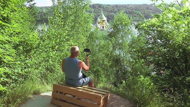 A male blogger with a mobile phone about travel talks about the temple from the back.