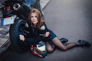 Fototapeta na wymiar The city streets and beauty young female biker with her own custom sport bike. Sunny photo of girl driver and modern motorcycle.