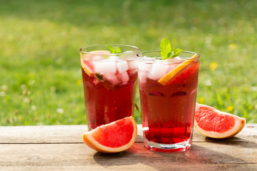 Fototapeta na wymiar Two glasess with grapefruit drinks, wooden table, green garden background