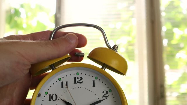 A retro clock that triggers the alarm and hand stops the alarm. Clock ringing in the morning at the bedroom and blurred windows in the background. Close up, selective focus