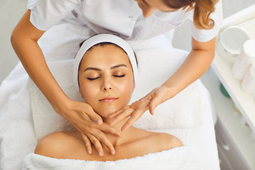 Beautician makes a facial massage to a woman in a spa salon. Woman receiving face protection...