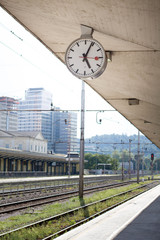 Train station clock on the platform with railroad tracks in the background, isolated.