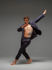 Stylish young guy dancer dancing in suit with naked torso isolated on gray background. Body with tattoo