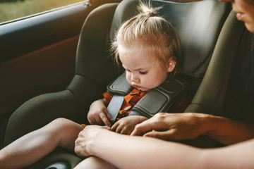 Child girl in safety car seat and mother fastens belt family road trip lifestyle vacations with baby security transportation