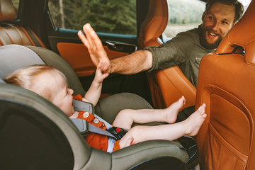 Father with child in car on road trip high five hands baby sitting in safety seat man driver family...