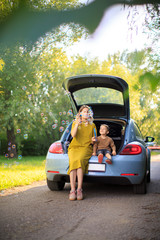 Beautiful mother and little son travelers sit in trunk of car on road and blow soap bubbles. Photo about family travel