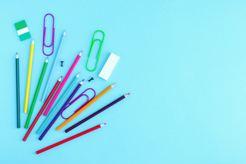 Stationery, crayons, stickers, eraser and paper clips scattered on a light blue background. Buying writing supplies, back to school, starting school.