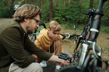 Fototapeta premium Adolescent boy in yellow hoodie and his father looking at chain of bicycle