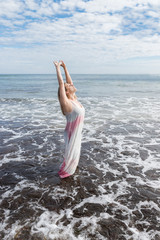 Woman in a dress in the sea enjoying her freedom with her arms up