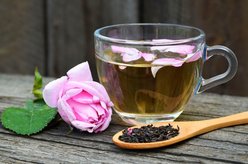 Rose herbal tea in a glass cup with pink petals and fresh flower on a rustic wooden table.Summer drinks, weight loss or diet concept.Selective focus.