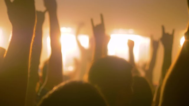 Slow motion: people crowd partying, cheering, raising hands up and clapping at rock concert in front of stage of nightclub. Bright colorful stage lighting. Nightlife and entertainment concept