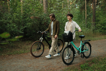 Fototapeta na wymiar Young cheerful man and woman in casualwear moving down road after cycling