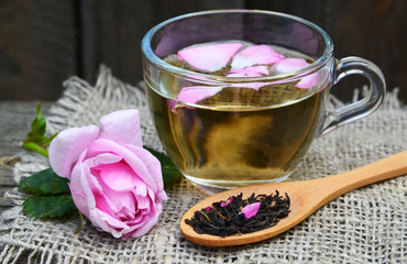 Rose herbal tea in a glass cup with pink petals and fresh flower on a rustic wooden table.Summer drinks, weight loss or diet concept.