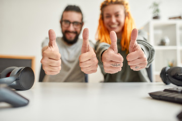 Cheerful man and woman showing thumbs up at camera. Young male and female technology blogger recording video blog or vlog about new gadgets at home