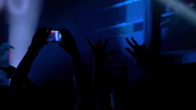 Slow motion: people hands silhouette taking photo or recording video of live music concert with smartphone. Crowd partying in front of stage. Photography, entertainment, technology concept
