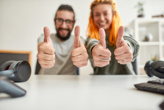 Cheerful man and woman showing thumbs up at camera. Young male and female technology blogger recording video blog or vlog about new gadgets at home