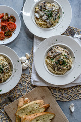 busy top down portrait photo of a traditional italian meal of mushroom pasta, side of tomatoes and garlic bread for 3