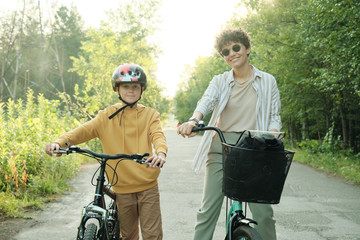 Young cheerful woman and her son having promenade on bicycles on summer day
