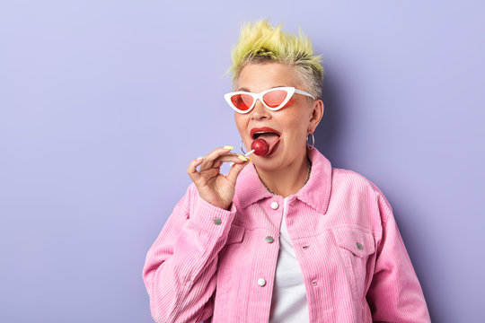 awesome fashion woman licking lollipop with tongue and posing to the camera. close up portrait. old granny takes pleasure in eating chupa chups