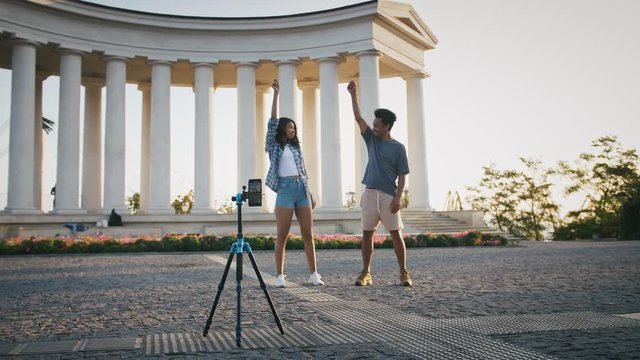 Ethnic black friends making videos for social network. Smiling, dancing in front of smartphone fixed on tripod in park