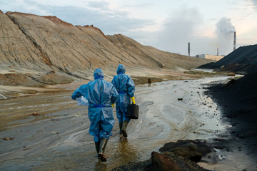 Rear view of two contemporary female scientists in blue protective coveralls