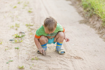 Boy draws with a stone on the sand while squatting on a sandy village road