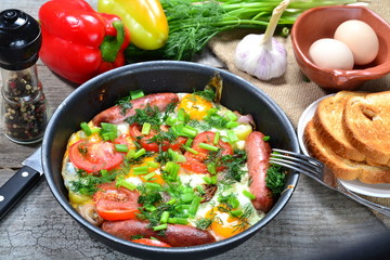 Scrambled eggs with fried sausages, onions, sweet red peppers, all in a frying pan.