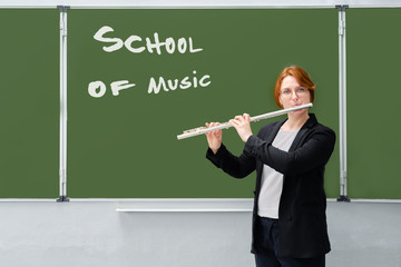 A music teacher plays the flute. Learning to play wind musical instruments against a blackboard with the text "Music School"