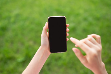 Girl using modern mobile phone with touch screen against green unfocused background. Black touch screen mockup