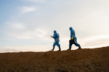 Two contemporary researchers in protective coveralls moving on top of hill