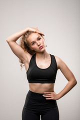 Fit young woman in black tracksuit touching her long blond curly hair