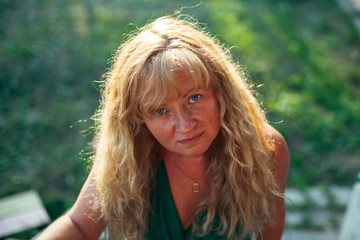Portrait of woman with light brown hair near a village house.