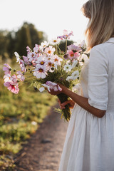 Back view of young woman with bouquet of flowers cosmos in hands. The concept of summer mood