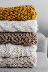 Detail of a stack of five woolen blankets of various colors beige, brown, white, hand-woven on a gray armchair.