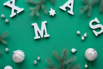 Creative Christmas flat lay with large white letters Xmas on green textile tablecloth. Fir twigs decorated with stars and mirror disco balls.