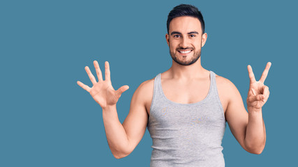 Fototapeta premium Young handsome man wearing swimwear and sleeveless t-shirt showing and pointing up with fingers number seven while smiling confident and happy.