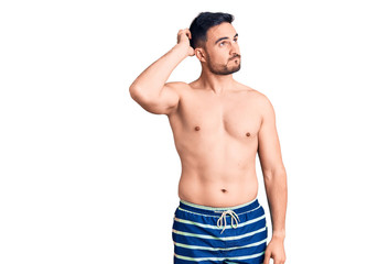 Fototapeta premium Young handsome man wearing swimwear confuse and wondering about question. uncertain with doubt, thinking with hand on head. pensive concept.