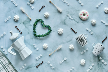Creative wintertime flat lay on light mint blue stone background. Ceramic coffee cups, coffee maker, sugar and sugar sticks. Sweets, doughnuts and marshmallows.