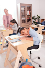 Mixed-race tired or bored schoolgirl in casualwear napping on desk at lesson